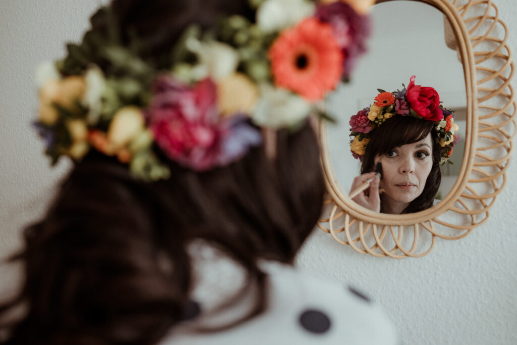 La future mariée se maquille chez elle devant le miroir avec sa couronne de fleurs sur la tête