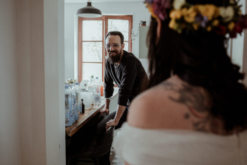 L'émotion et le sourire du futur marié qui découvre sa femme dans sa robe de mariée avec une couronne de fleurs sur la tête.