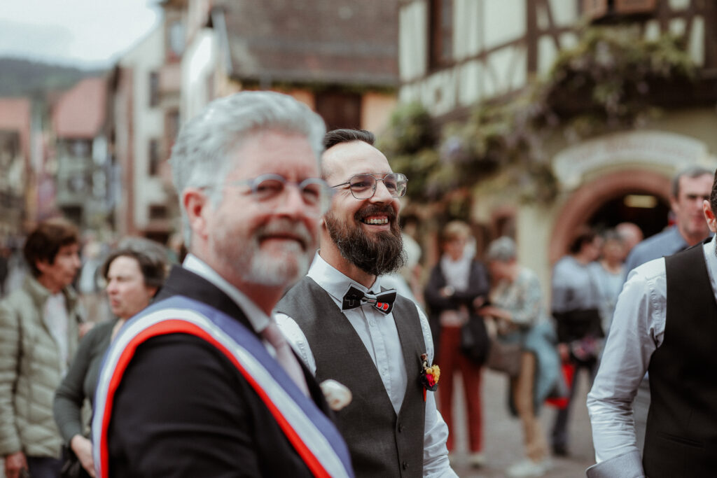 Le marié au milieu de ses invités et du maire de Riquewihr avant d'entrer à la mairie pour son mariage près de Colmar en Alsace