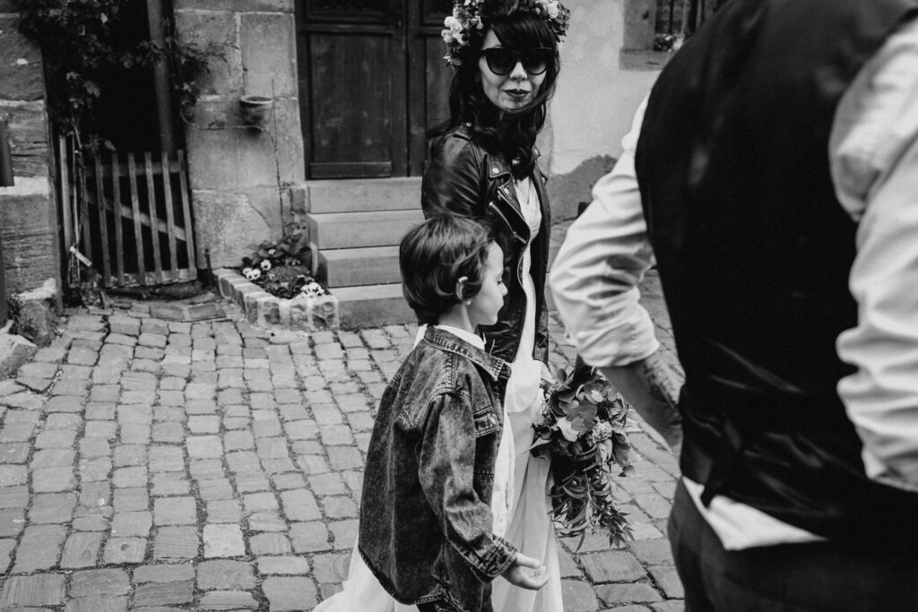 Mariée dans sa robe de mariée en perfecto noir et avec une couronne de fleurs sur la tête dans les rues de Riquewihr en Alsace près de Colmar pour son mariage