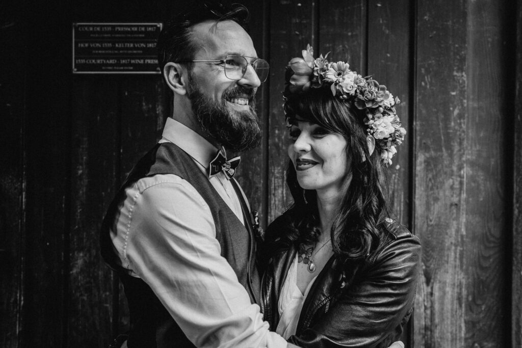 Photo de couple des mariés qui rient ensemble. La mariée a une couronne de fleurs sur la tête et un perfecto noir