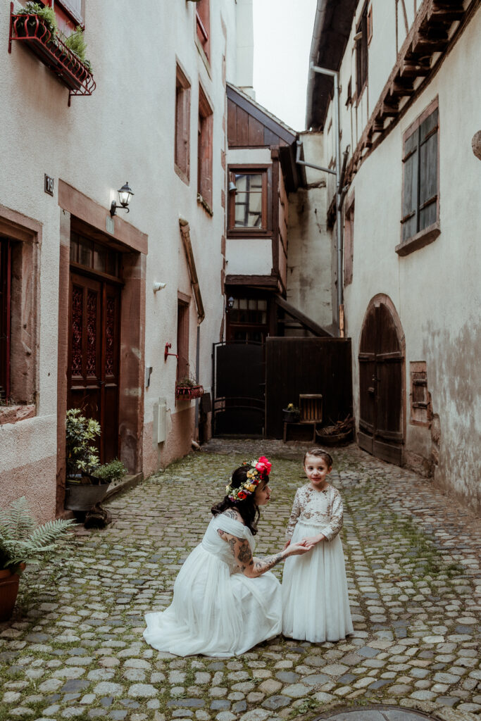 Mariée dans sa robe et avec sa couronne de fleurs sur la tête, avec sa fille en robe blanche pour le mariage dans ses parents dans les rues de Riquewihr près de Colmar en Alsace